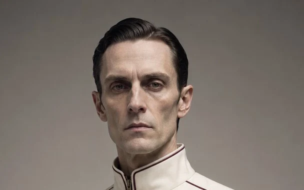 Caldus Rime, a pale dark-haired man in a cream technical uniform